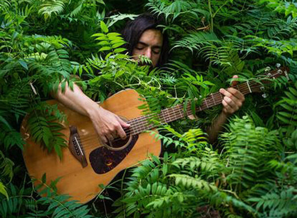 photo of pete moss playing guitar surrounded by green foliage